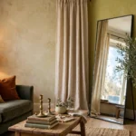 Budget luxury living room with limewash walls, velvet cushions, brass lamp and candlesticks, a large leaning mirror and an olive tree